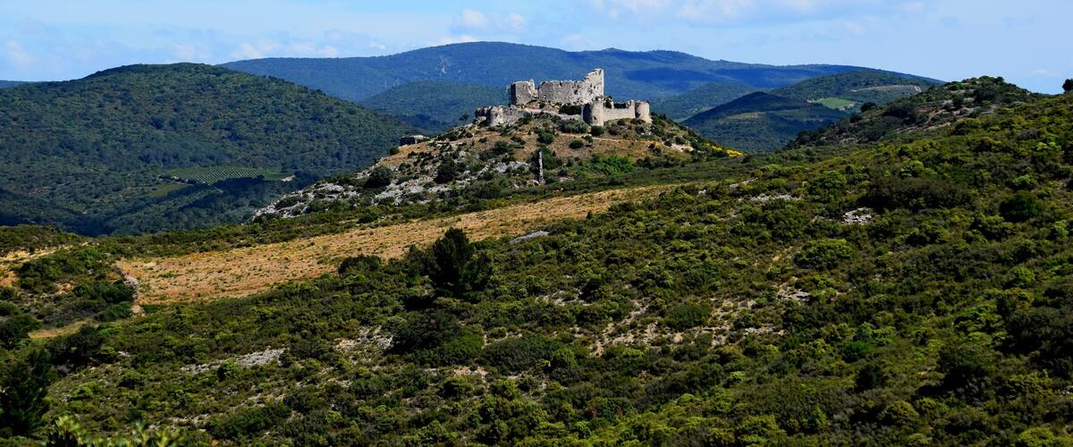 A castle on a hill surrounded by lush green hills and a clear blue sky.