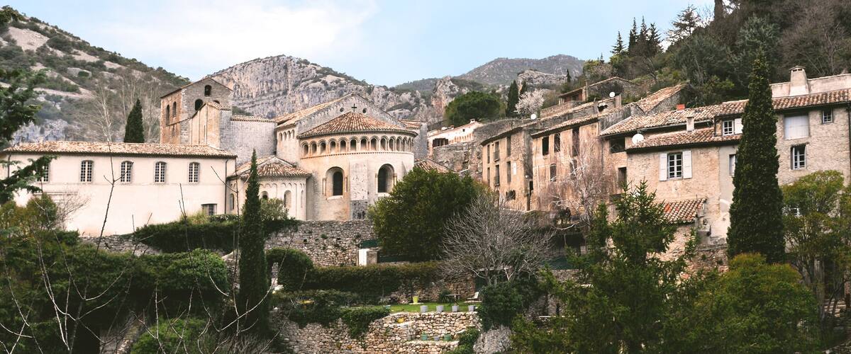 A historic town with stone buildings, a prominent church, and a mountainous backdrop.