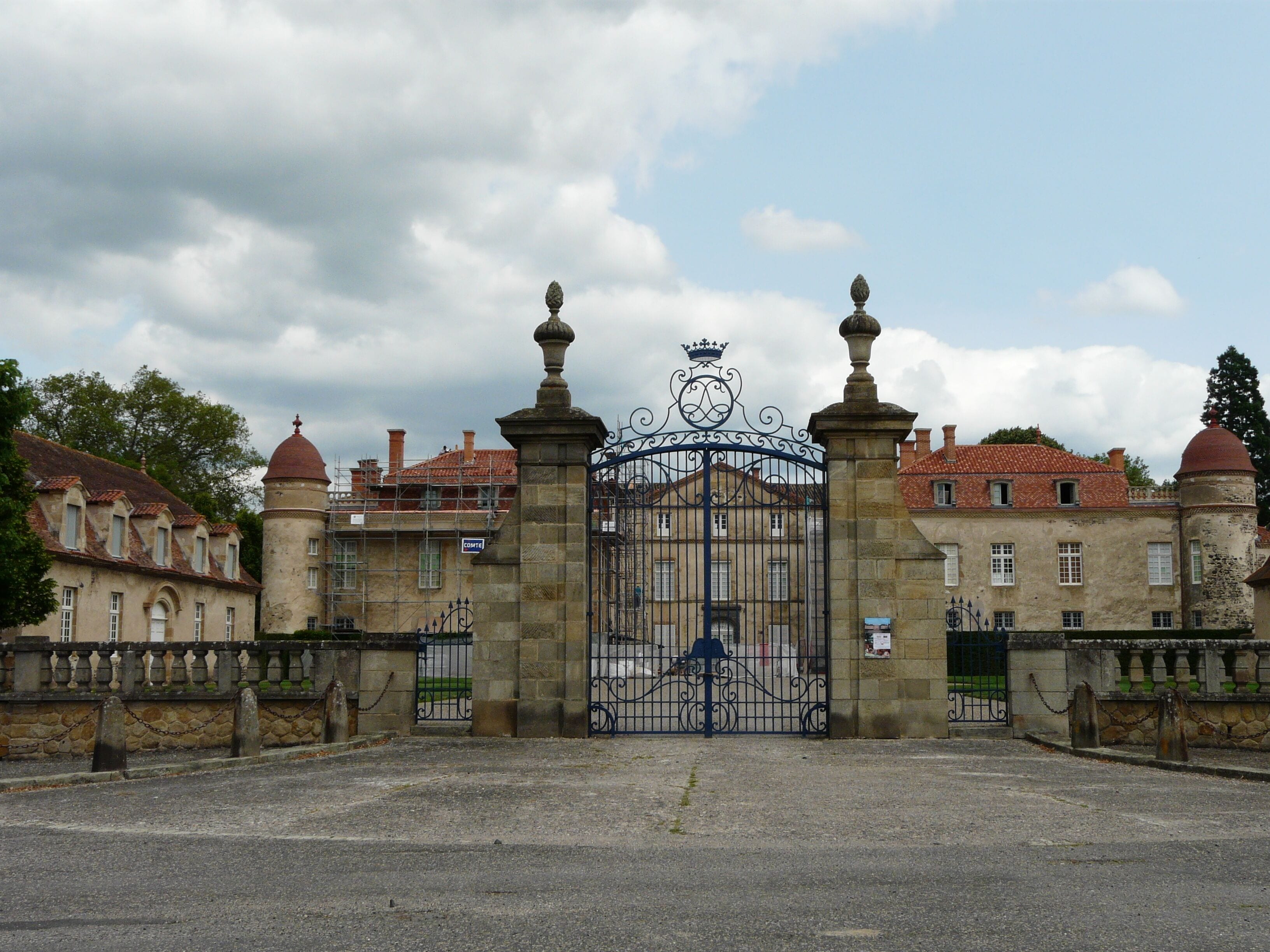 A historic building with a large ornate gate, a tower, and a red-tiled roof.