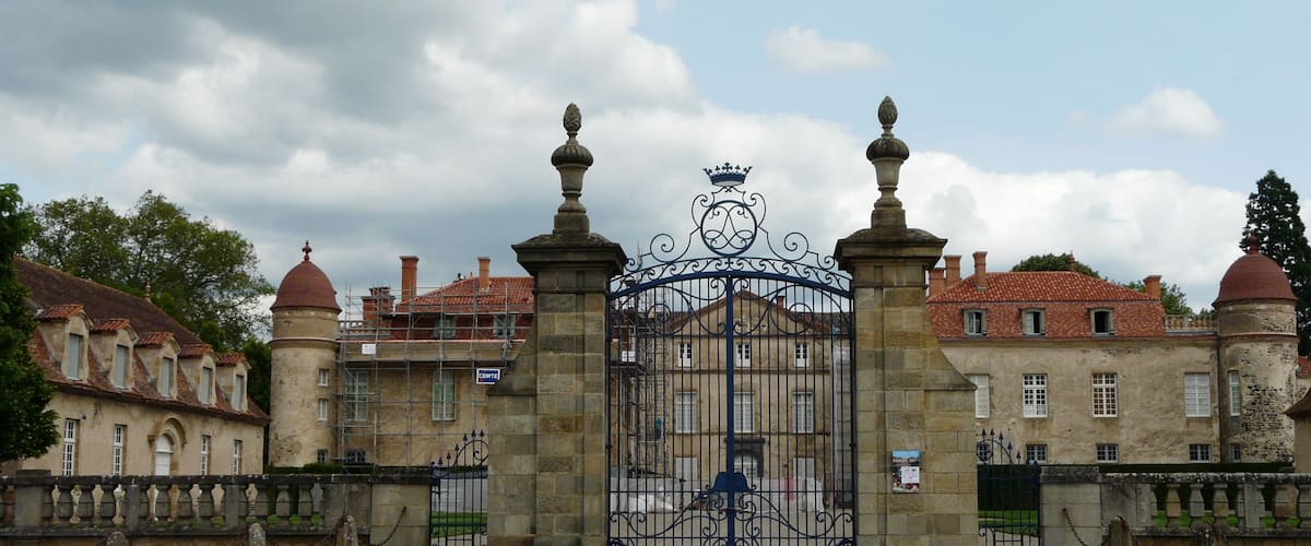 A historic building with a large ornate gate, a tower, and a red-tiled roof.