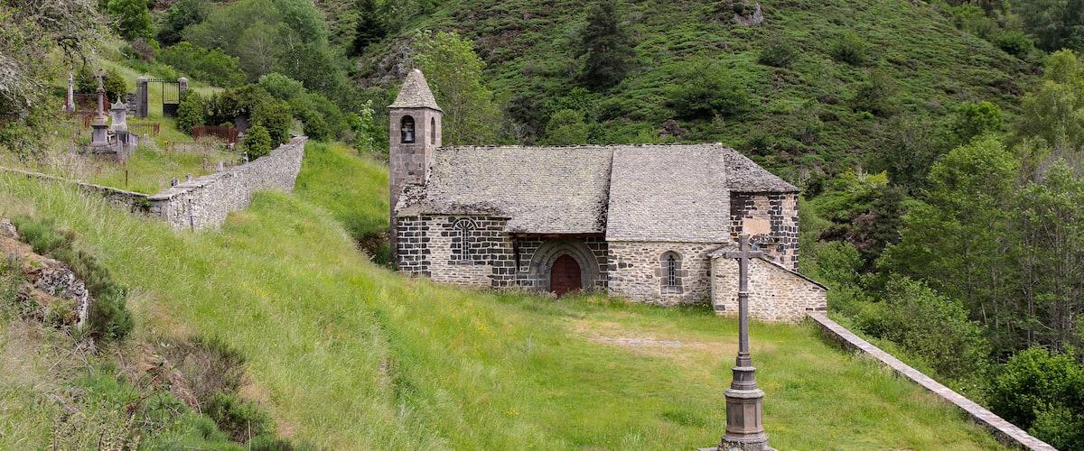 A stone church with a bell tower on a grassy hillside.