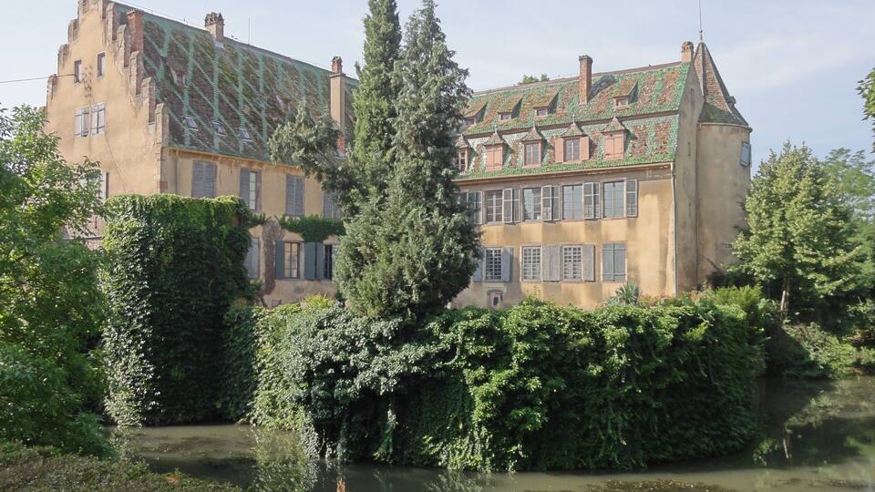 A large, historic building with a green roof and ivy-covered walls.