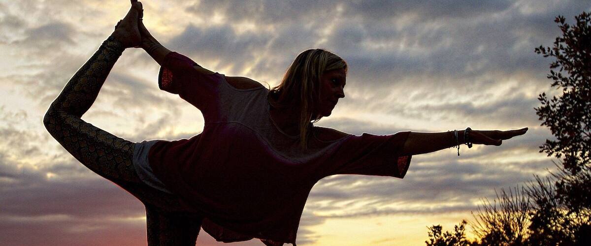 A person performing a yoga pose against a sunset sky.