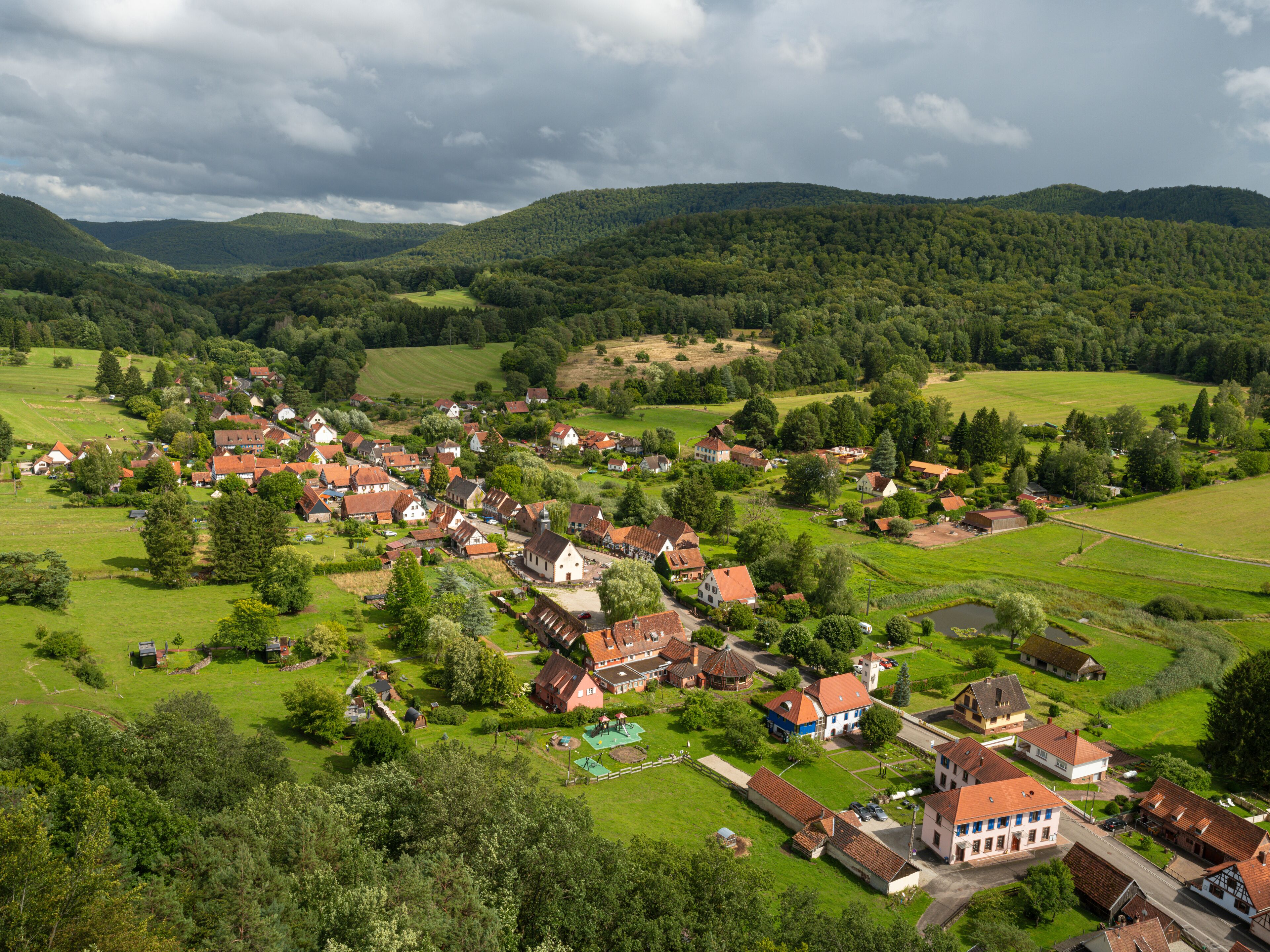 A picturesque village nestled in a valley with lush greenery, surrounded by rolling hills and a dense forest.