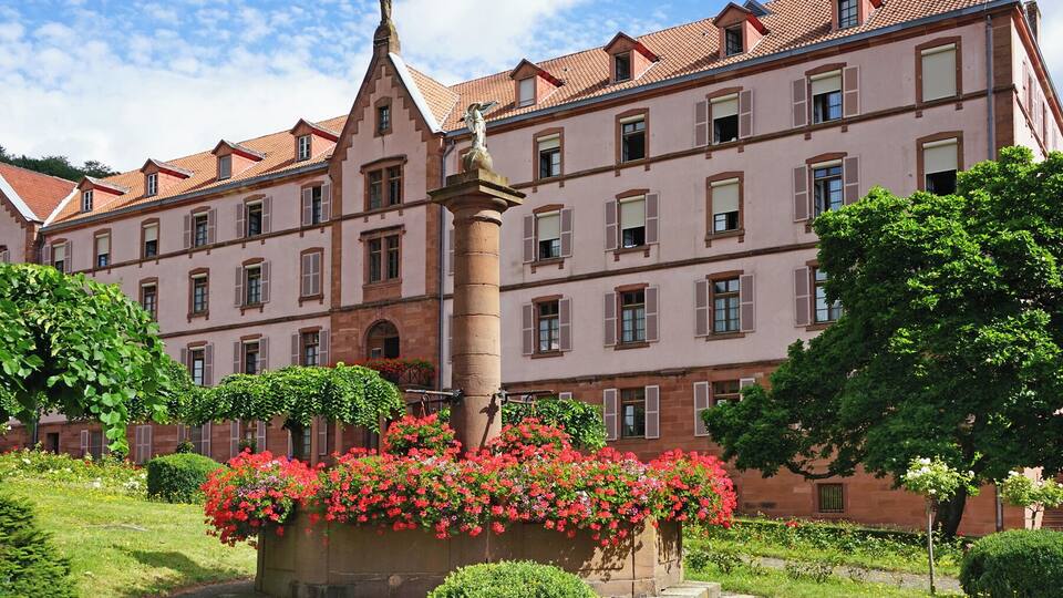 A historic building with a statue, red flowers, and a well-maintained garden.