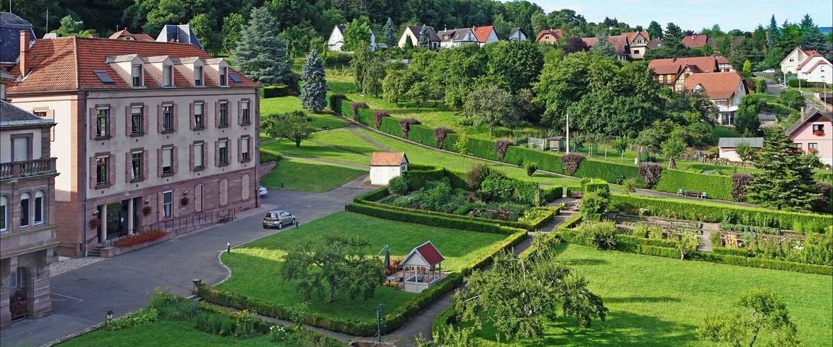 A lush green landscape with a large building, neatly trimmed hedges, and a variety of trees.