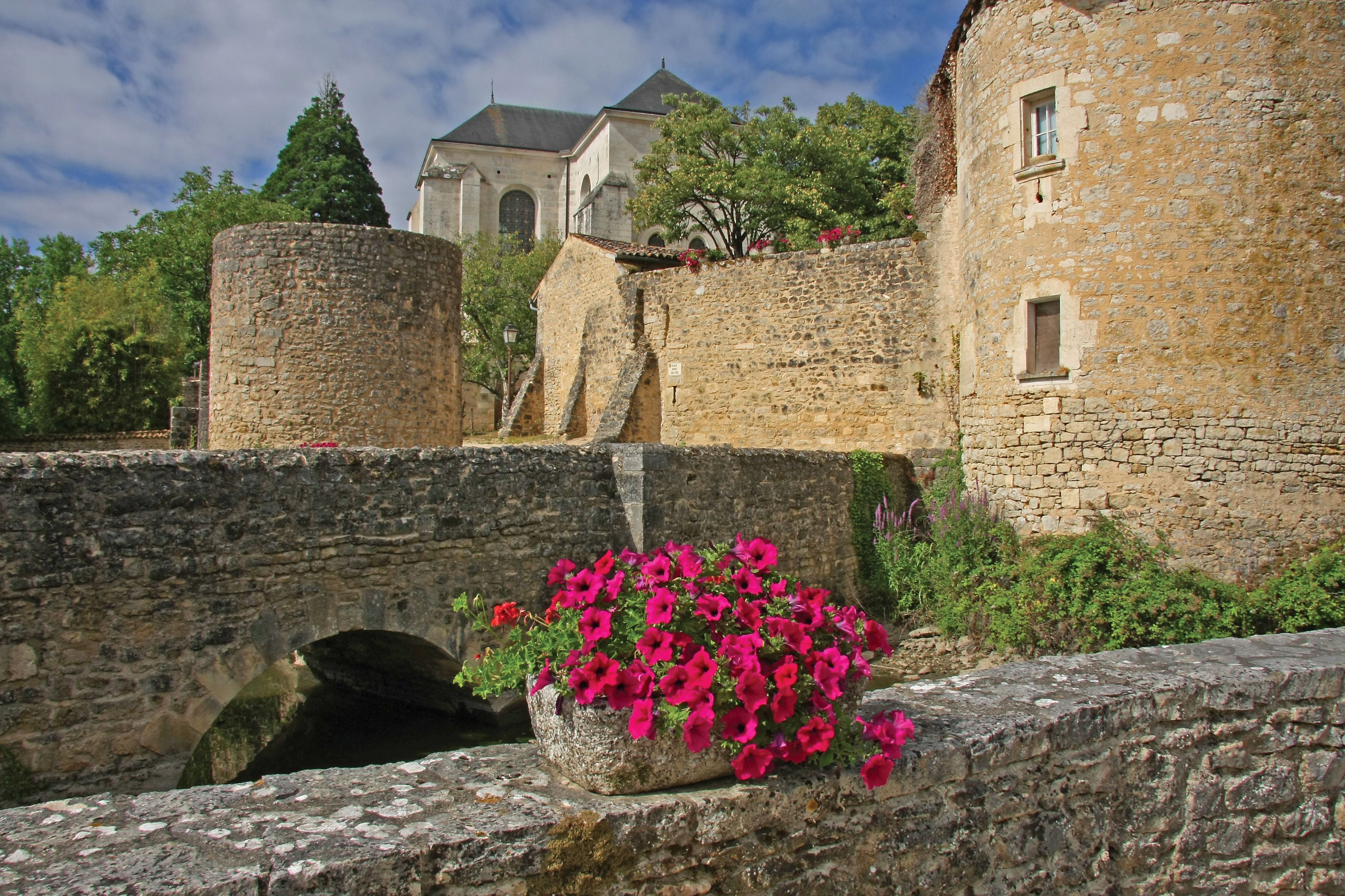 A stone bridge with a flower pot, a stone wall, and a building with a tower in the background.