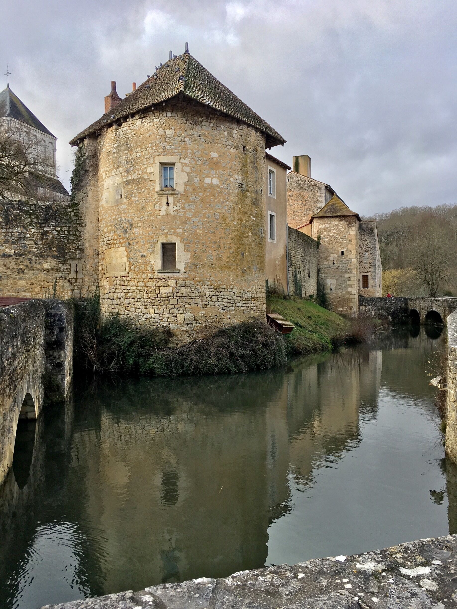 A stone building with a tiled roof near a calm river.
