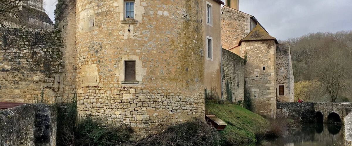 A stone building with a tiled roof near a calm river.