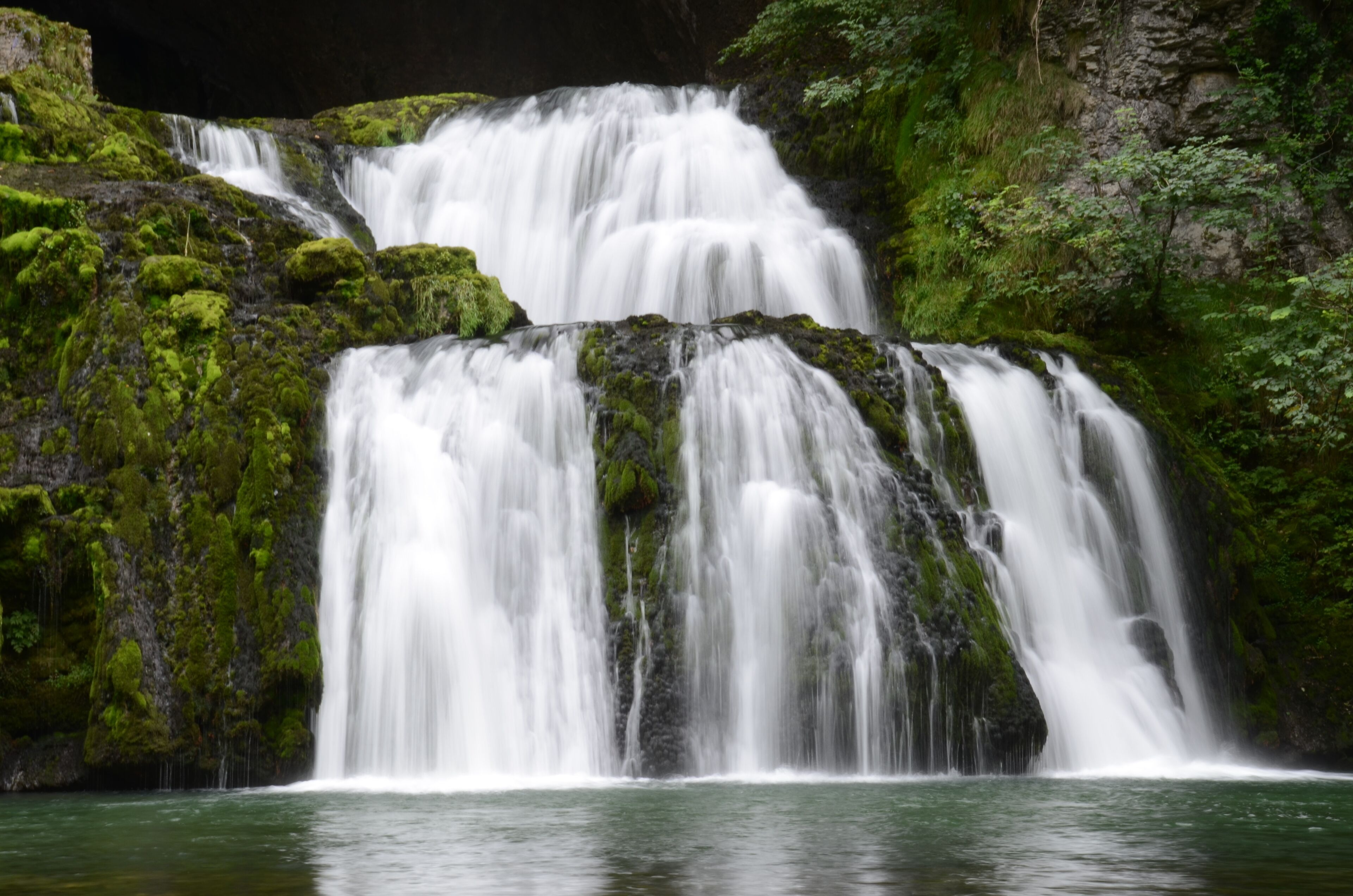 A multi-tiered waterfall surrounded by lush green moss and rocks.