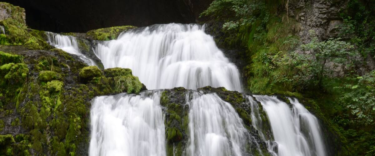 A multi-tiered waterfall surrounded by lush green moss and rocks.