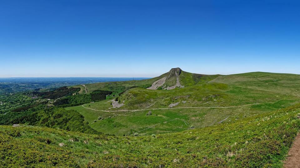 A mountain with a distinct peak, a winding trail, and a valley with scattered buildings.