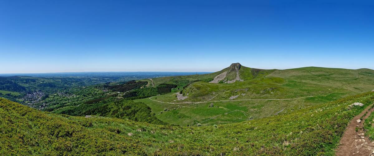 A mountain with a distinct peak, a winding trail, and a valley with scattered buildings.