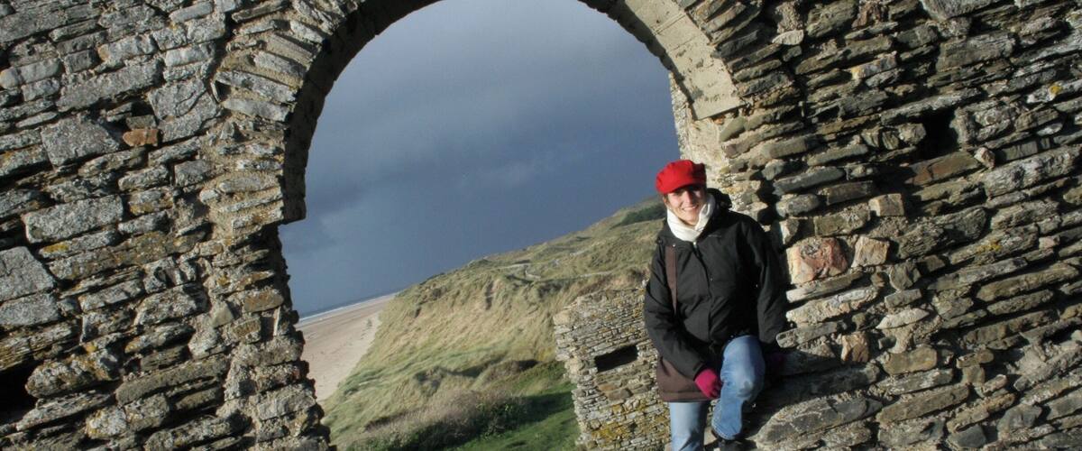 A person sitting in a stone archway overlooking a grassy hill.