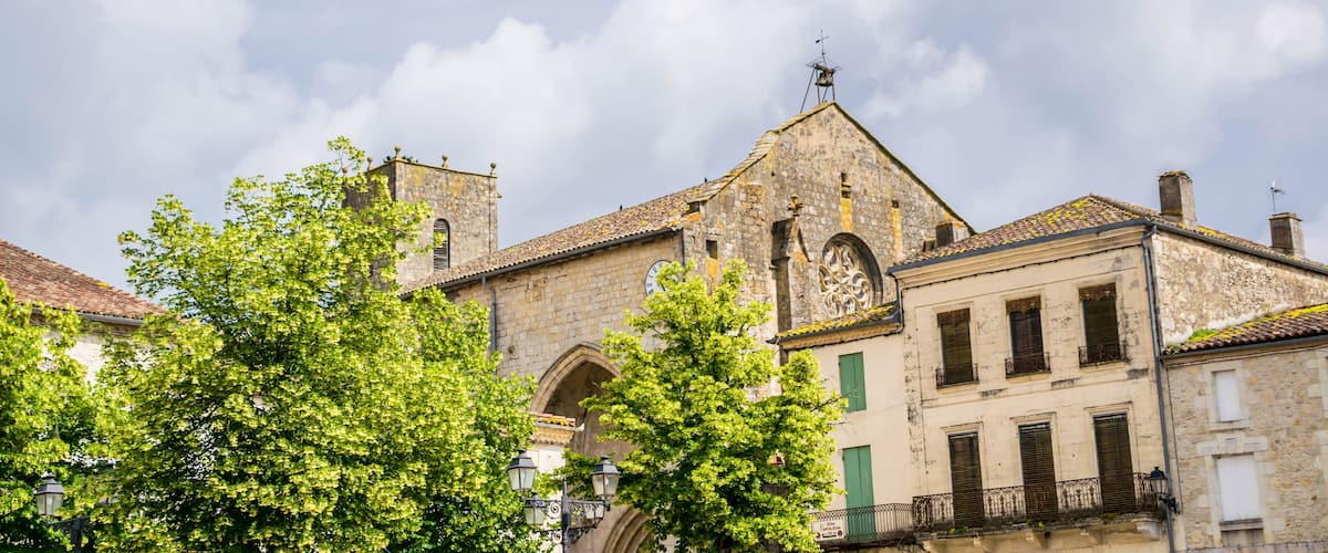A historic stone building with a clock tower, surrounded by lush green trees.