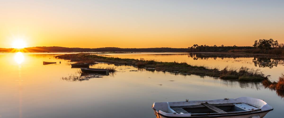 A calm lake at sunset with a small boat in the foreground and a distant shoreline.