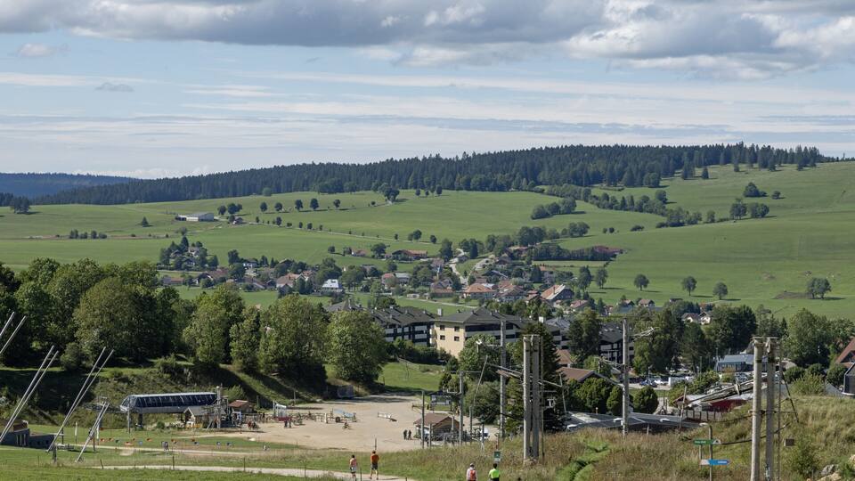 A rural landscape with rolling hills, a small village, and a sports field.