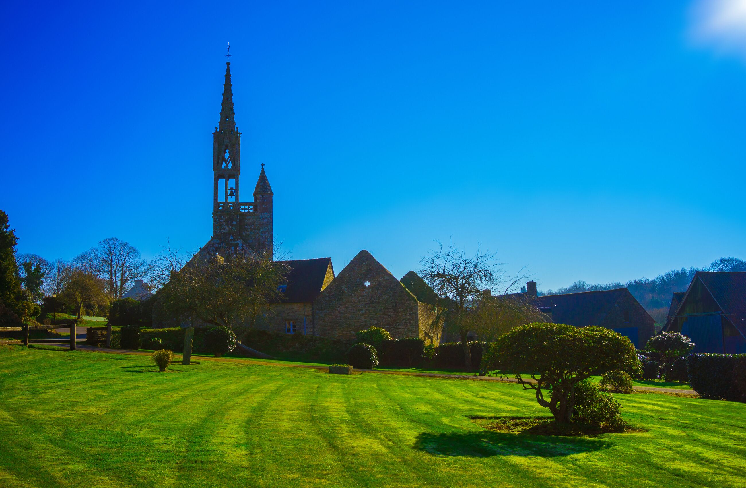 A church with a tall spire, surrounded by a well-maintained lawn and stone buildings.