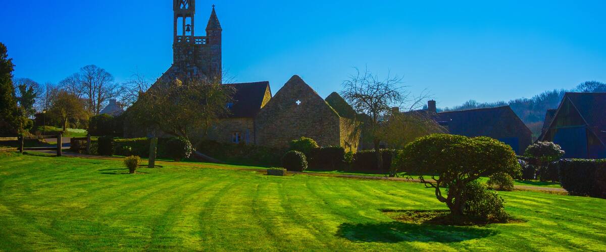 A church with a tall spire, surrounded by a well-maintained lawn and stone buildings.