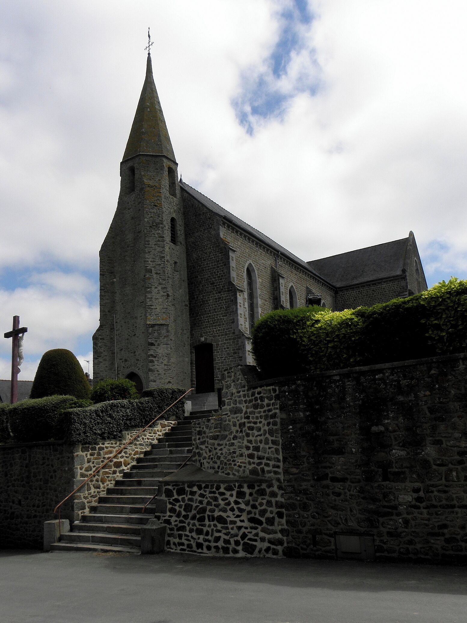 A stone church with a tall steeple and a cross at the top.