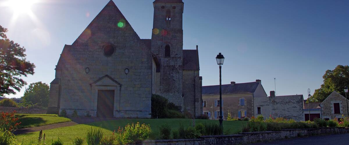 A stone church with a tall tower and a weather vane, surrounded by greenery and a clear sky.