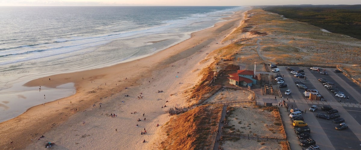 A beach with people, a parking lot, and a building with a red roof.