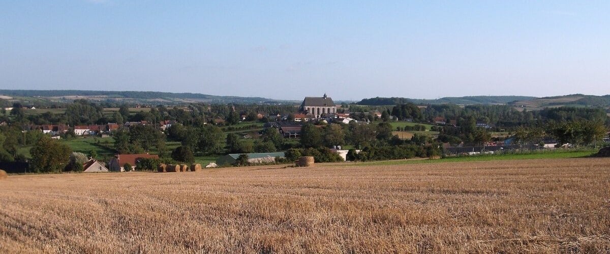A rural landscape with a field of crops, a church, and scattered houses.