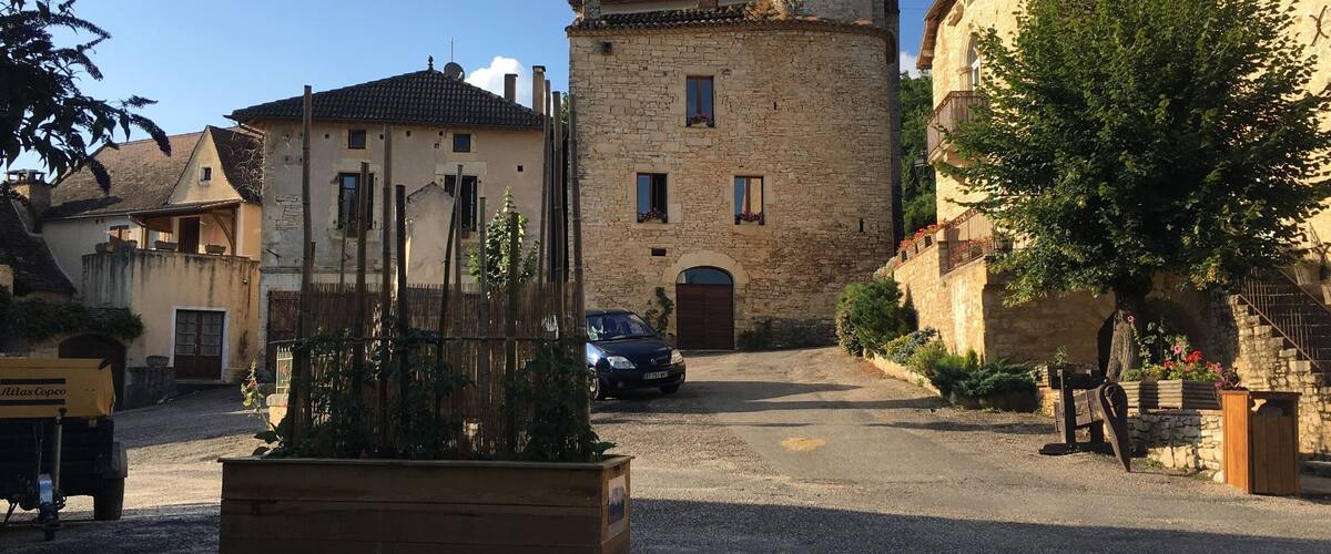 A stone tower, a wooden building, and a parked car in a village street.