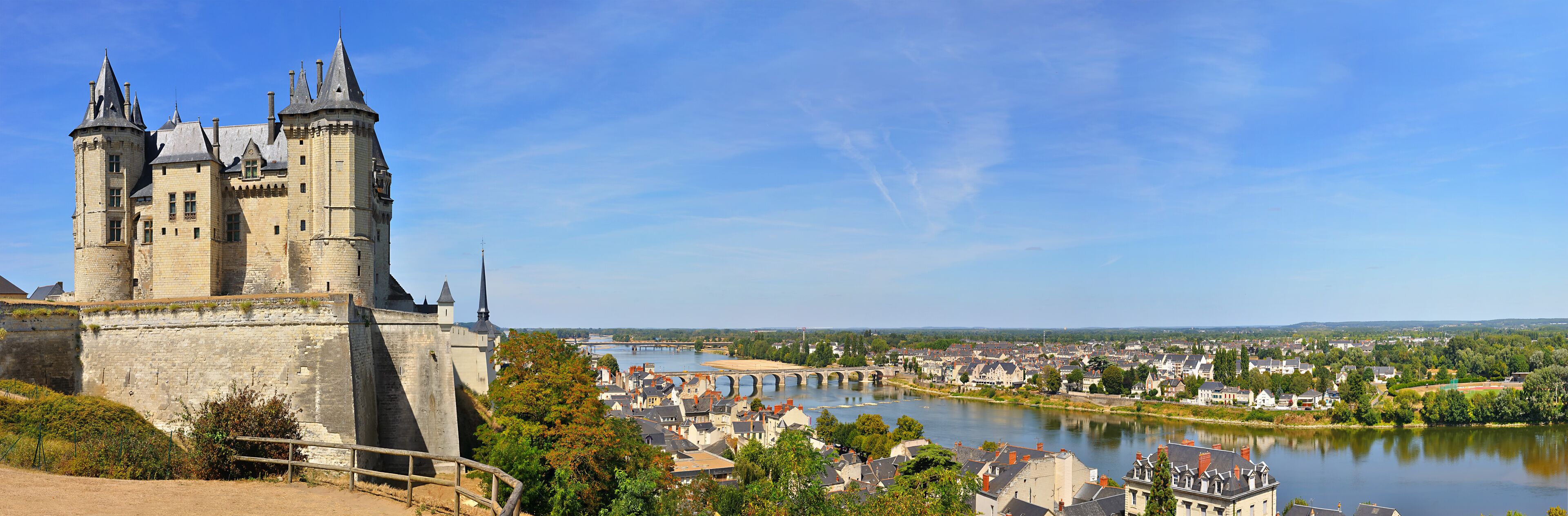 A historic castle with multiple towers overlooking a river and a town.