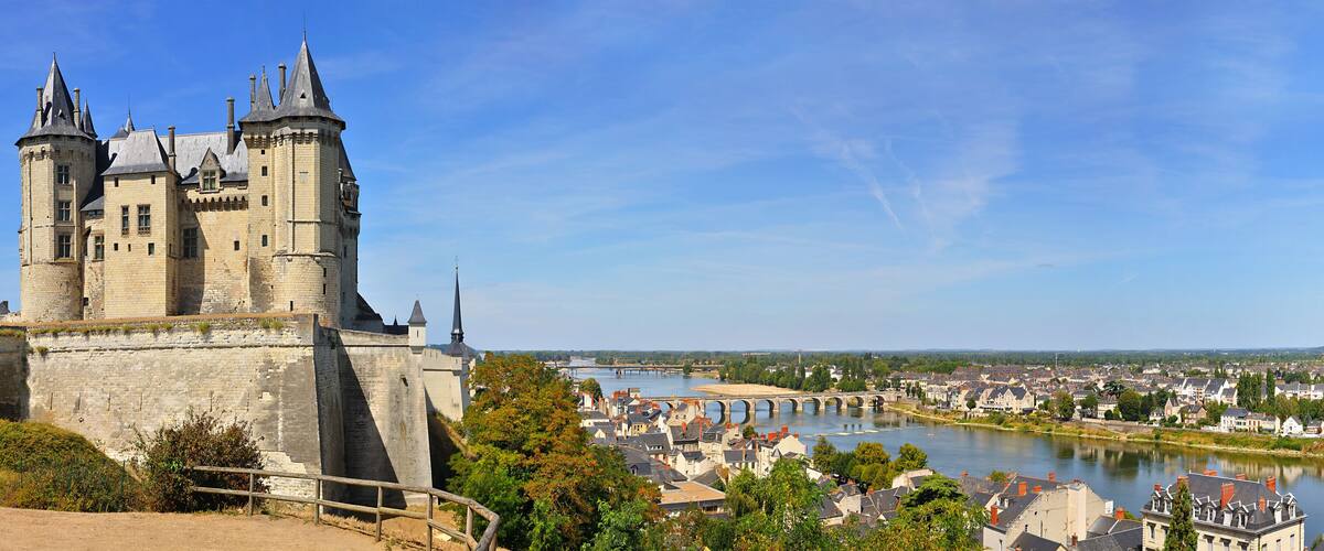 A historic castle with multiple towers overlooking a river and a town.