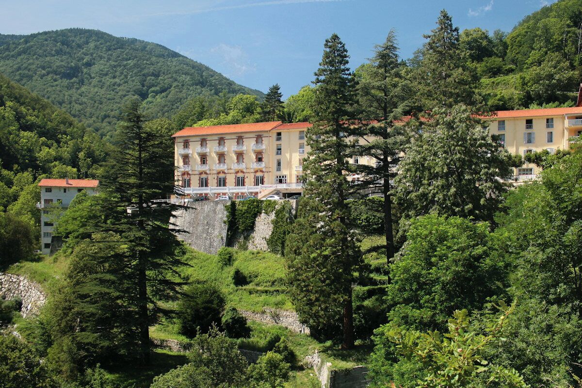 A hillside building with a red roof, surrounded by lush greenery and trees.