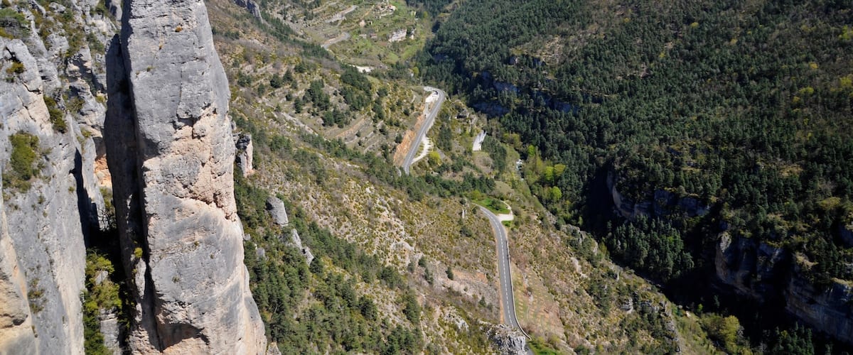 A mountainous landscape with a winding road, rocky cliffs, and dense forest.