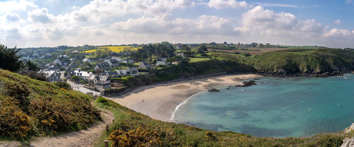 A coastal town with a sandy beach, clear blue waters, and lush green hills.