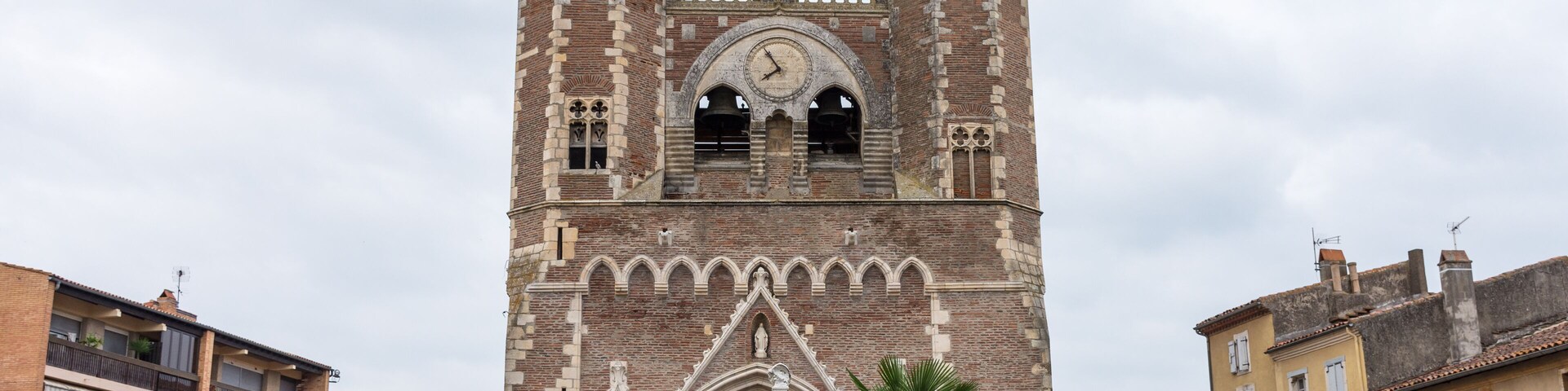 Una torre histórica con un reloj, dos estatuas y un arco de color rojo.