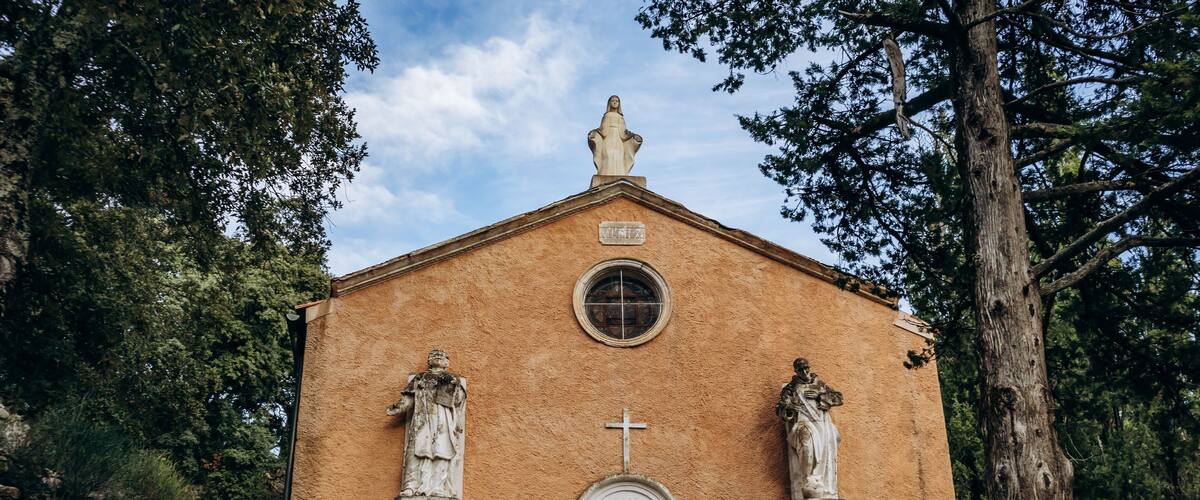 A small church with a cross, statues, and a stone wall.