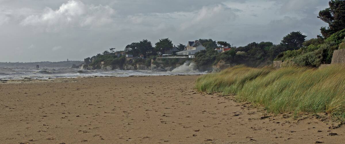 A sandy beach with waves crashing onto the shore, a grassy cliff, and houses on a hillside.
