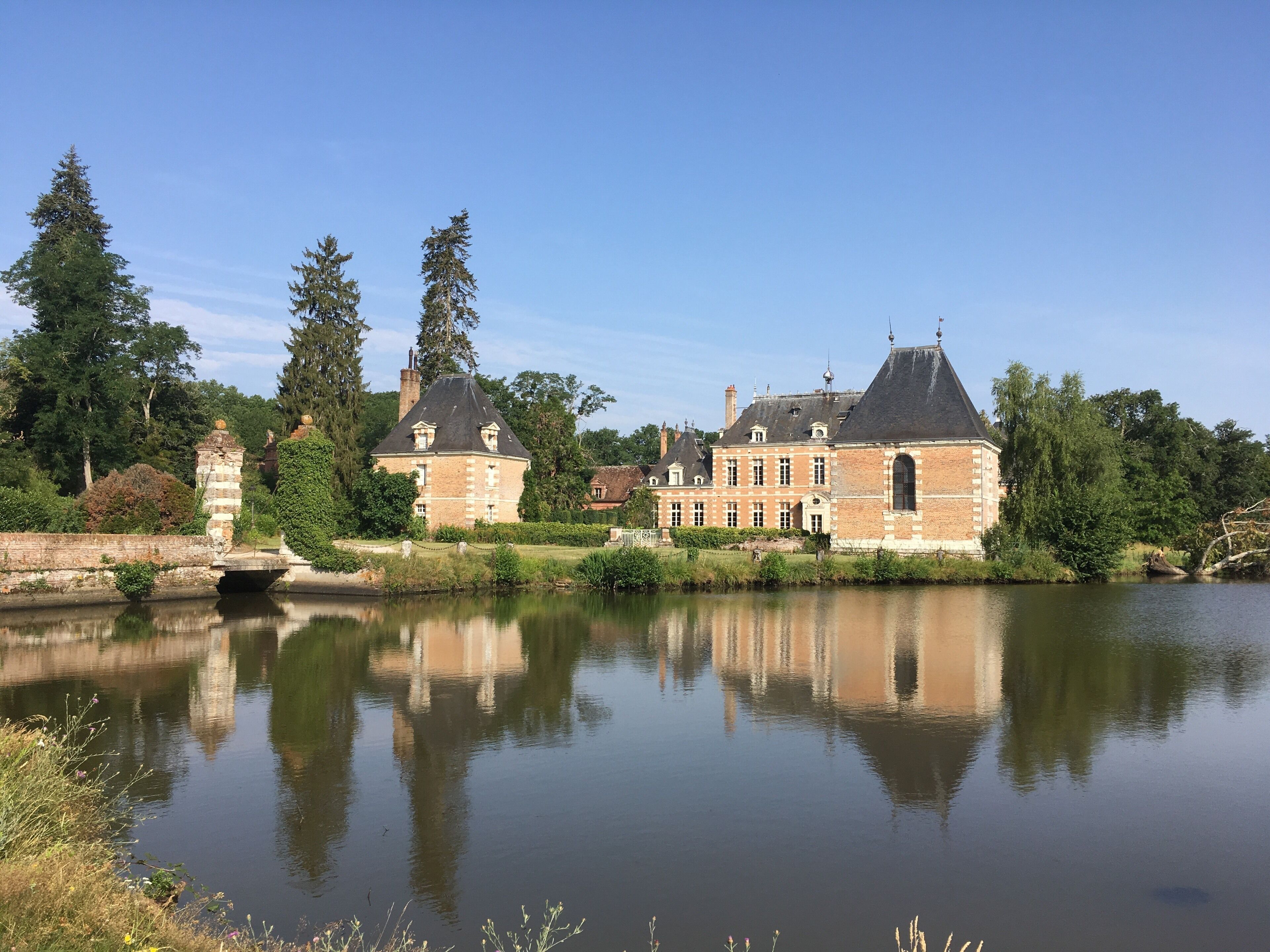 A large brick building with a pond in front, surrounded by trees and greenery.