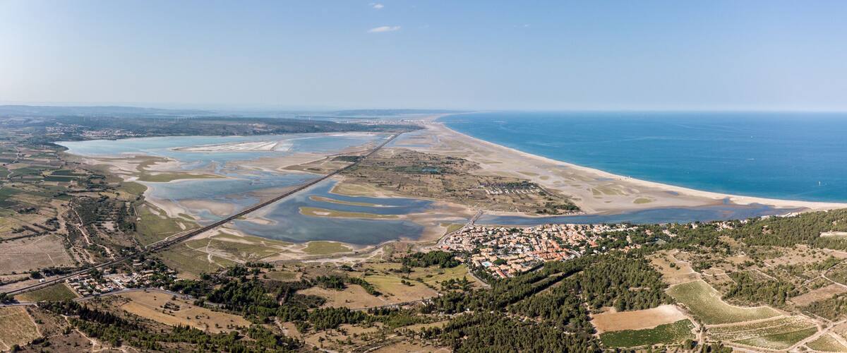 An aerial view of a coastal town with a beach, a river, and agricultural fields.