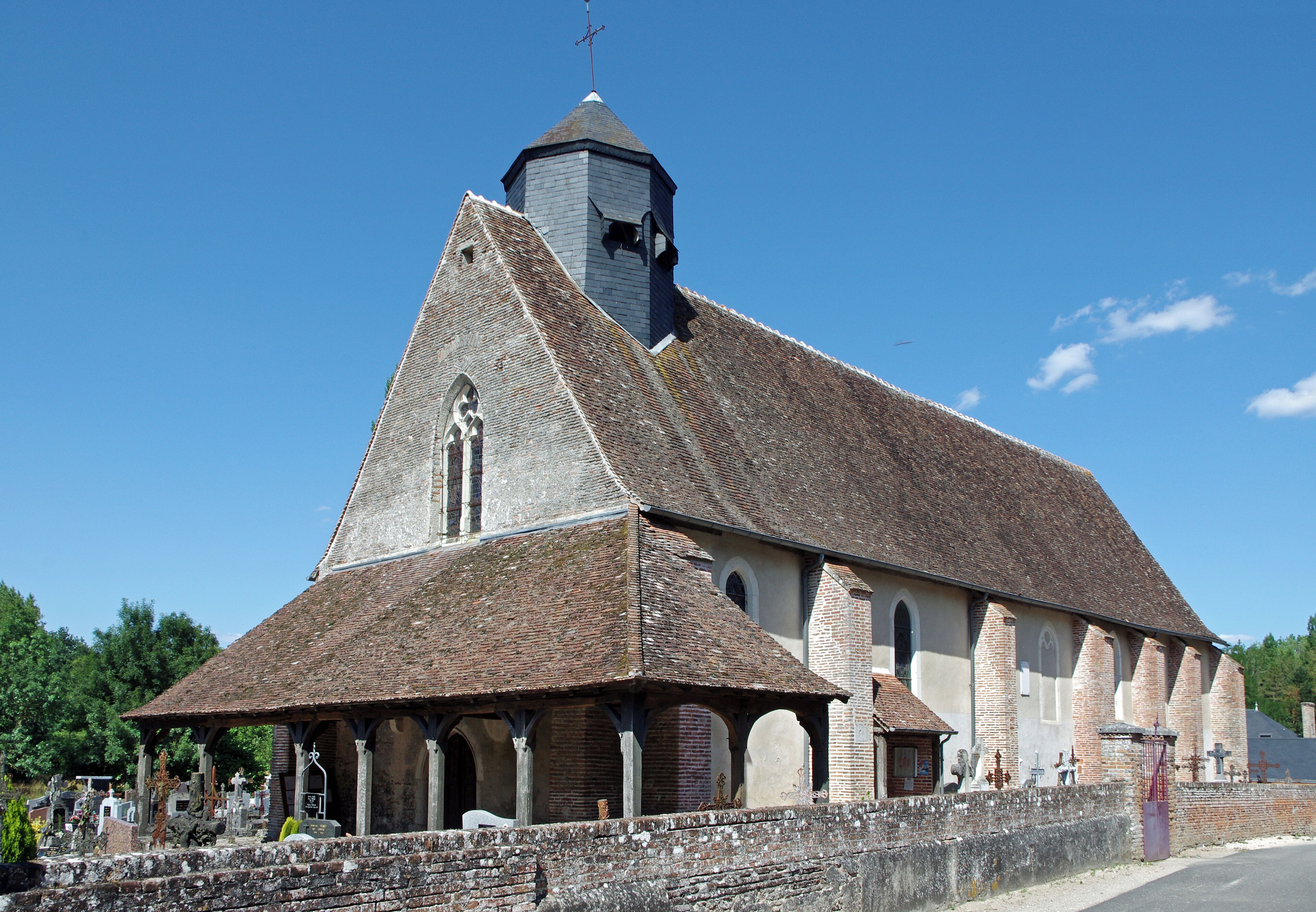 A church with a bell tower, a covered porch, and a cemetery in front.