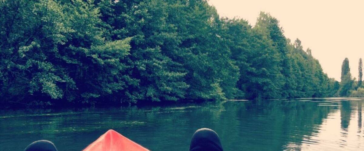A kayak on a calm river surrounded by dense green trees.