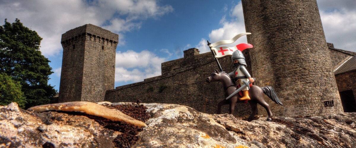 A medieval castle with a large tower and a knight statue holding a flag.