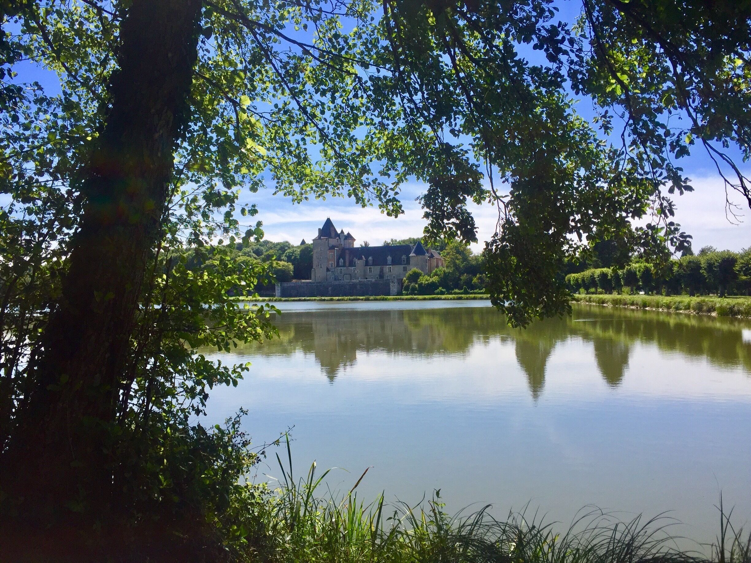 A castle by a calm lake surrounded by trees.