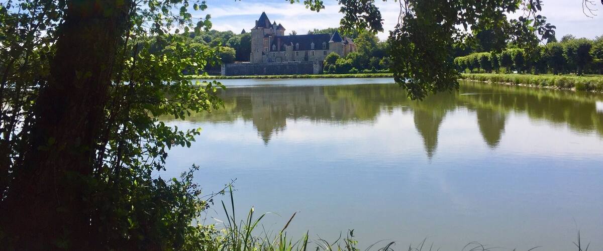A castle by a calm lake surrounded by trees.