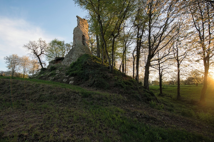 A stone ruin on a grassy hill with trees in the background.