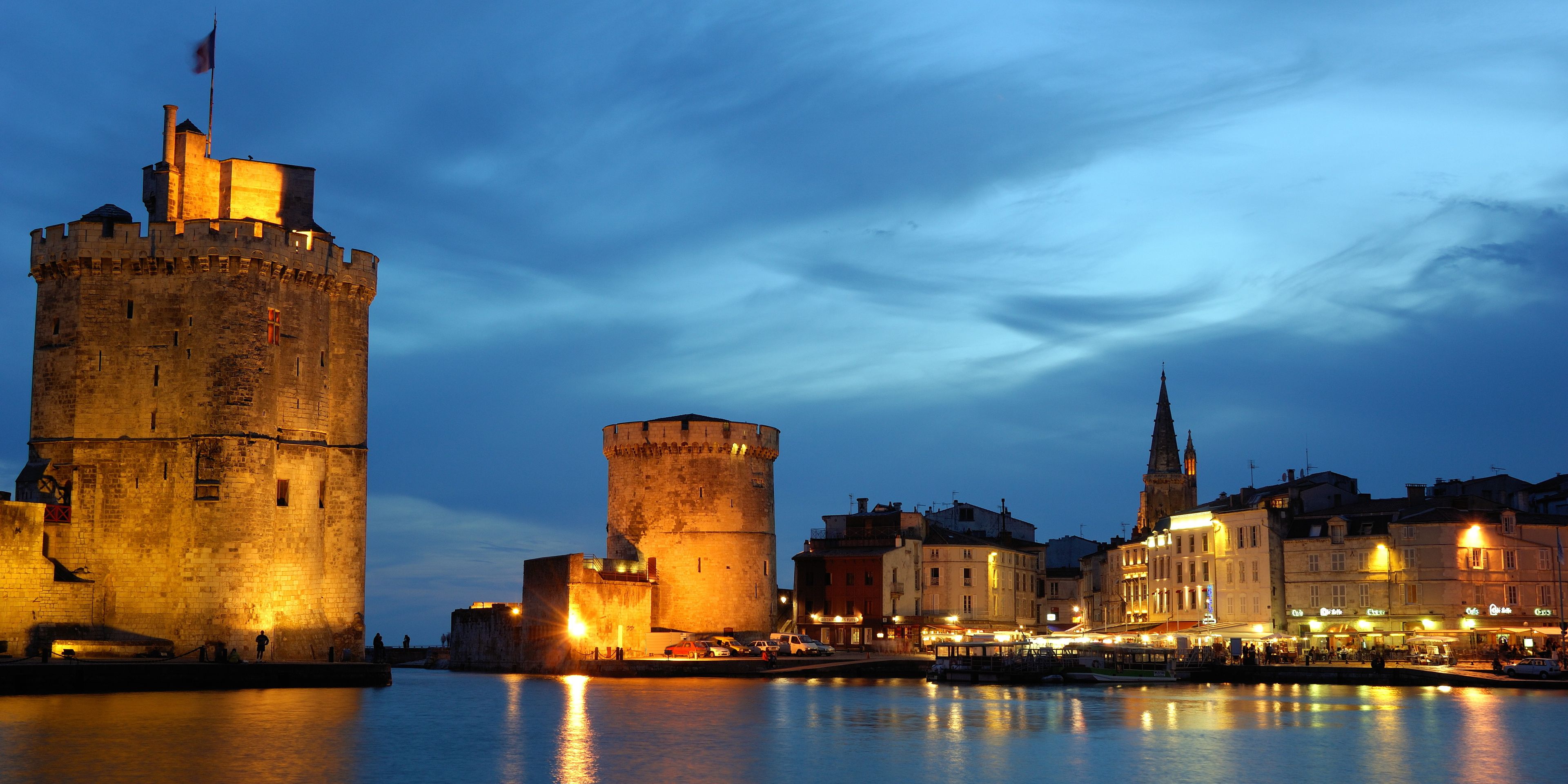 Un paysage urbain historique, avec des tours et des bâtiments illuminés le long du front de mer.