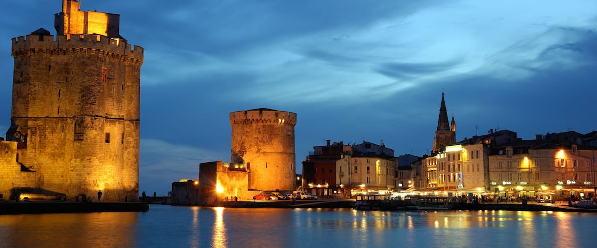 Un paysage urbain historique, avec des tours et des bâtiments illuminés le long du front de mer.