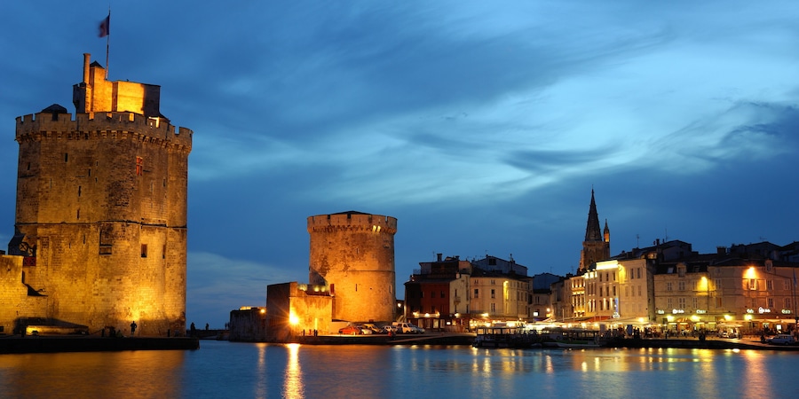 Un paysage urbain historique, avec des tours et des bâtiments illuminés le long du front de mer.