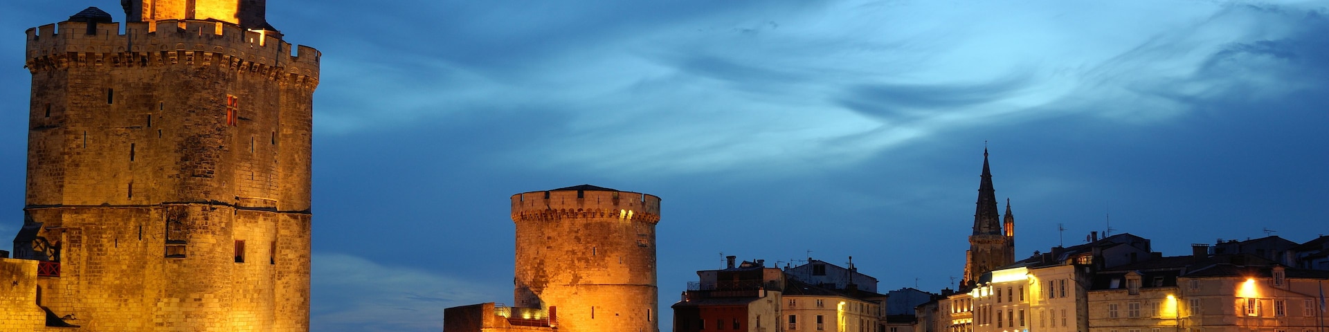 Un paysage urbain historique, avec des tours et des bâtiments illuminés le long du front de mer.