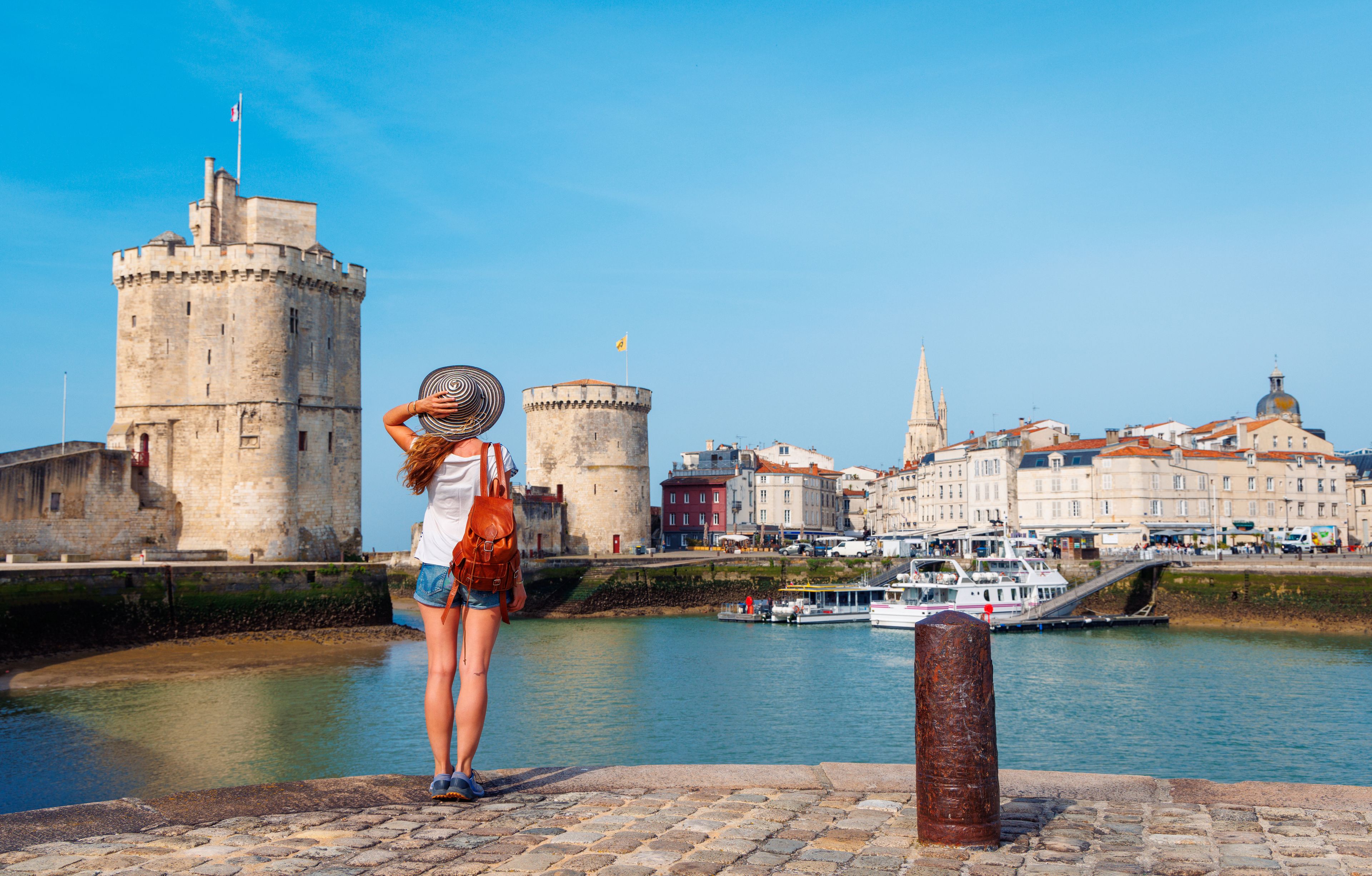A historic stone tower, a river with boats, and a cityscape with buildings.