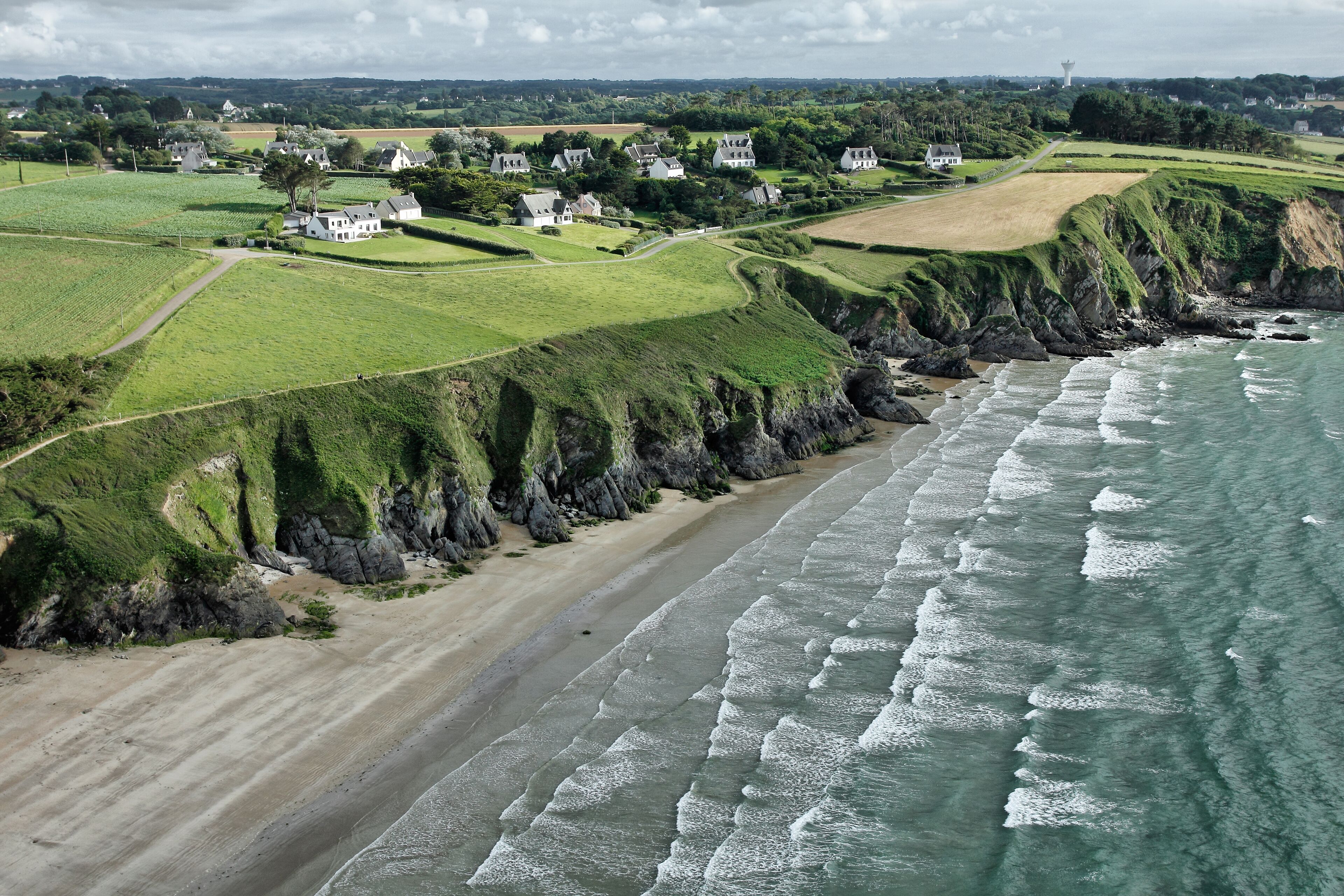 A coastal village with houses on grassy hills, a sandy beach, and the ocean.